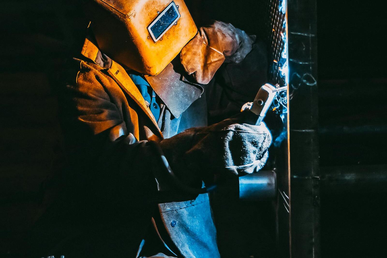 Certified TIG welder performing precision welding on steel fabrication with bright arc and protective helmet at The High Road Manufacturing